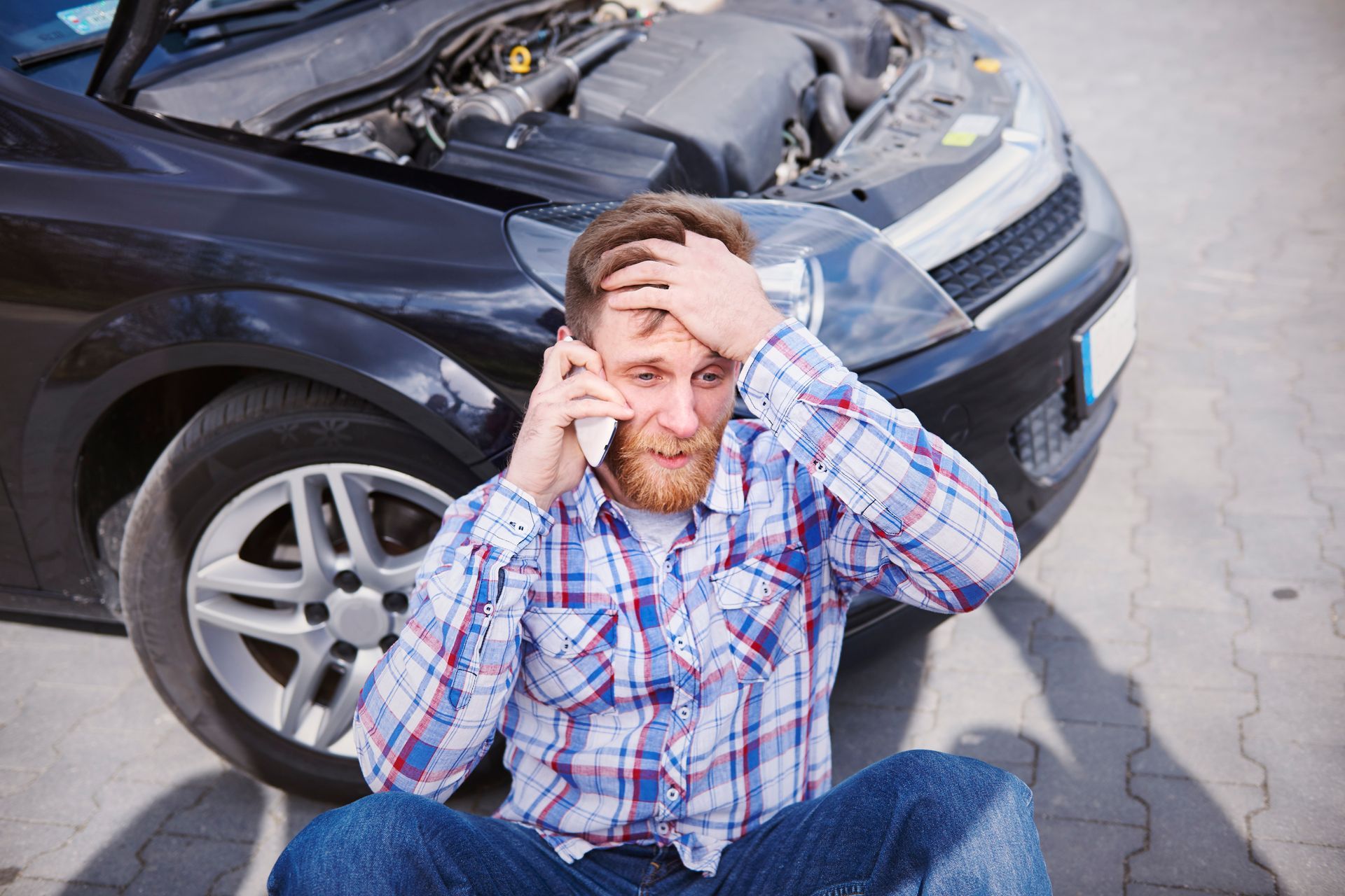 Man sitting on the road beside a crashed black car, holding his head in distress