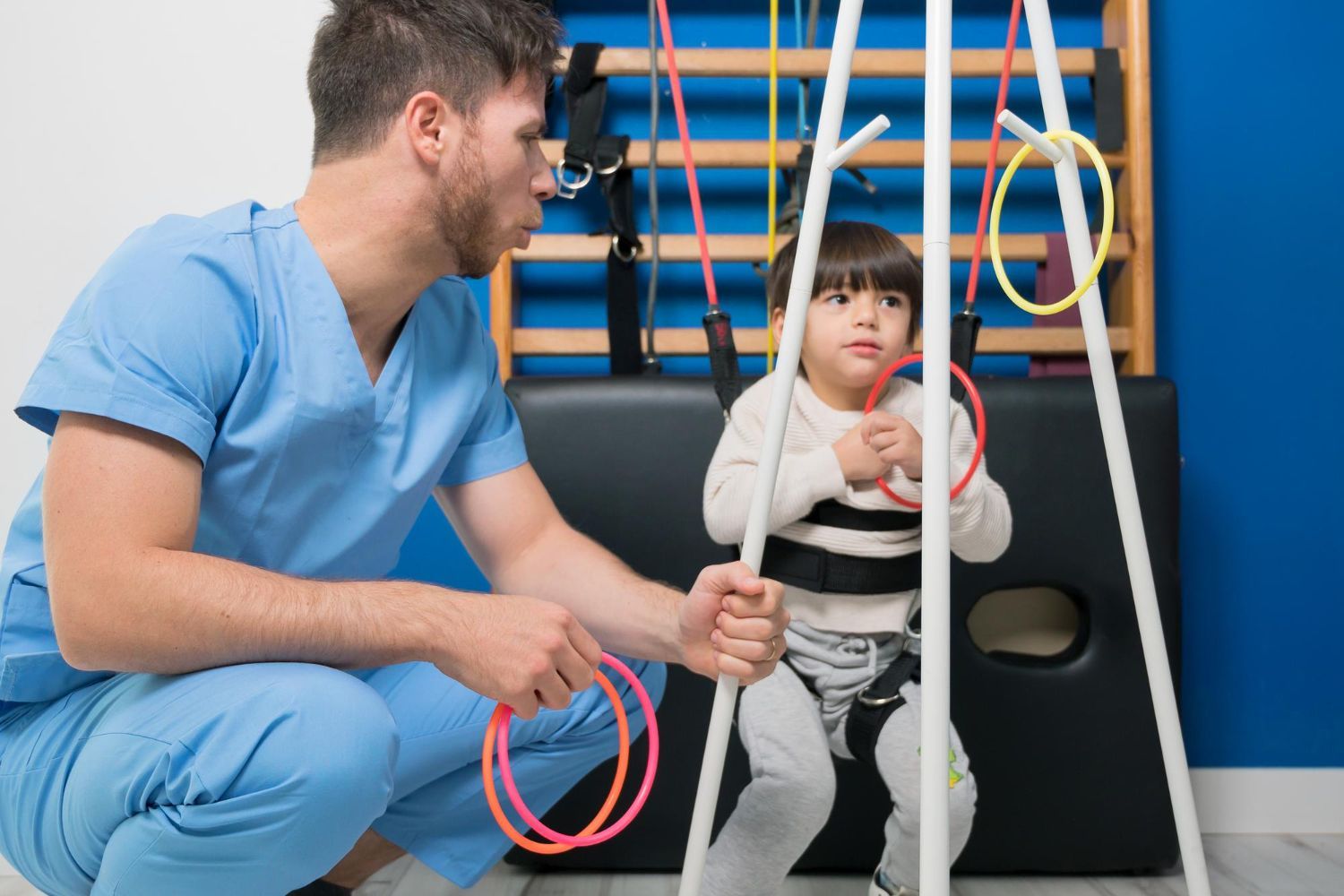 A man is kneeling down next to a little boy sitting on a swing.
