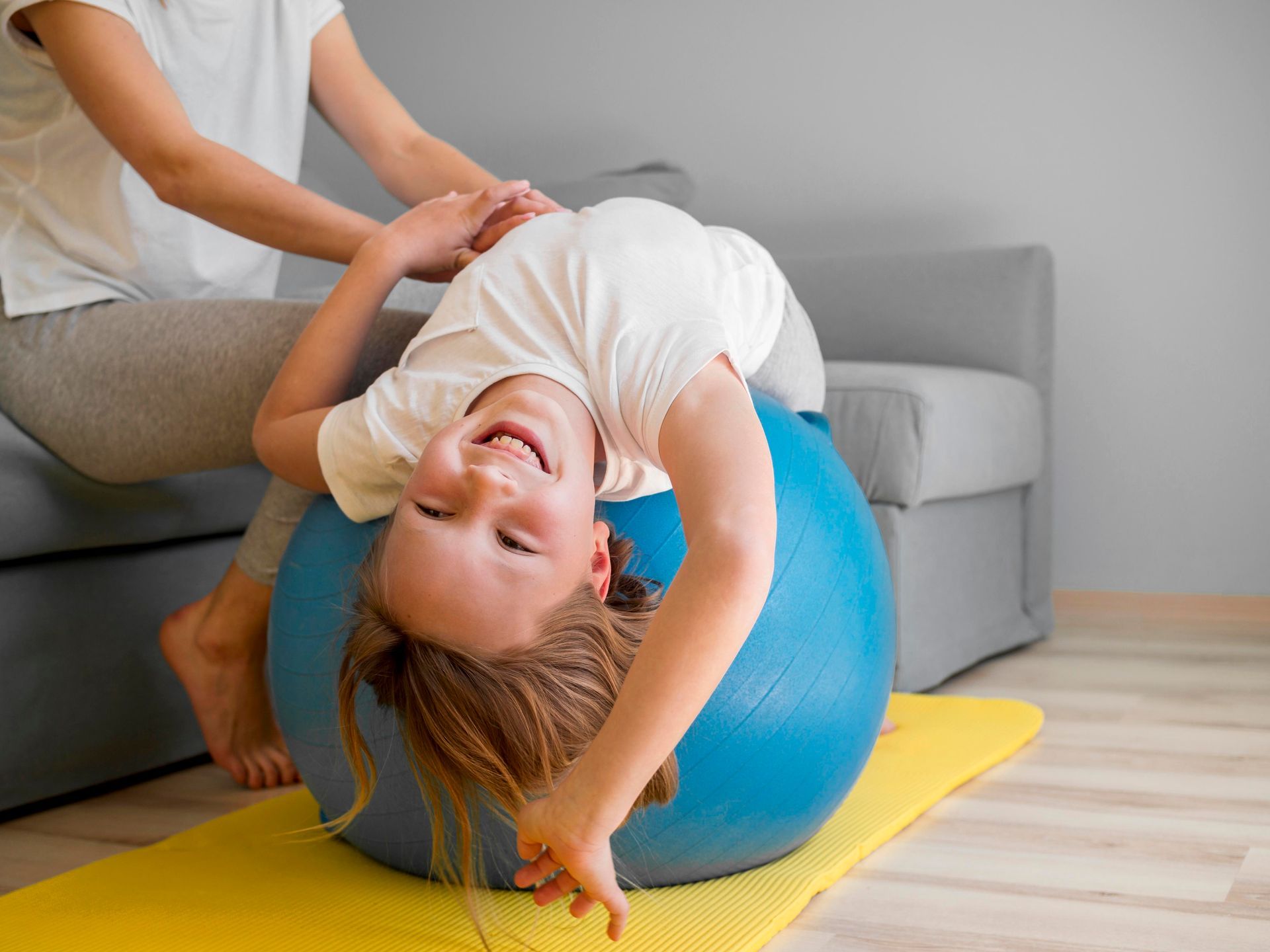 A little girl is playing with a blue exercise ball on a yoga mat.