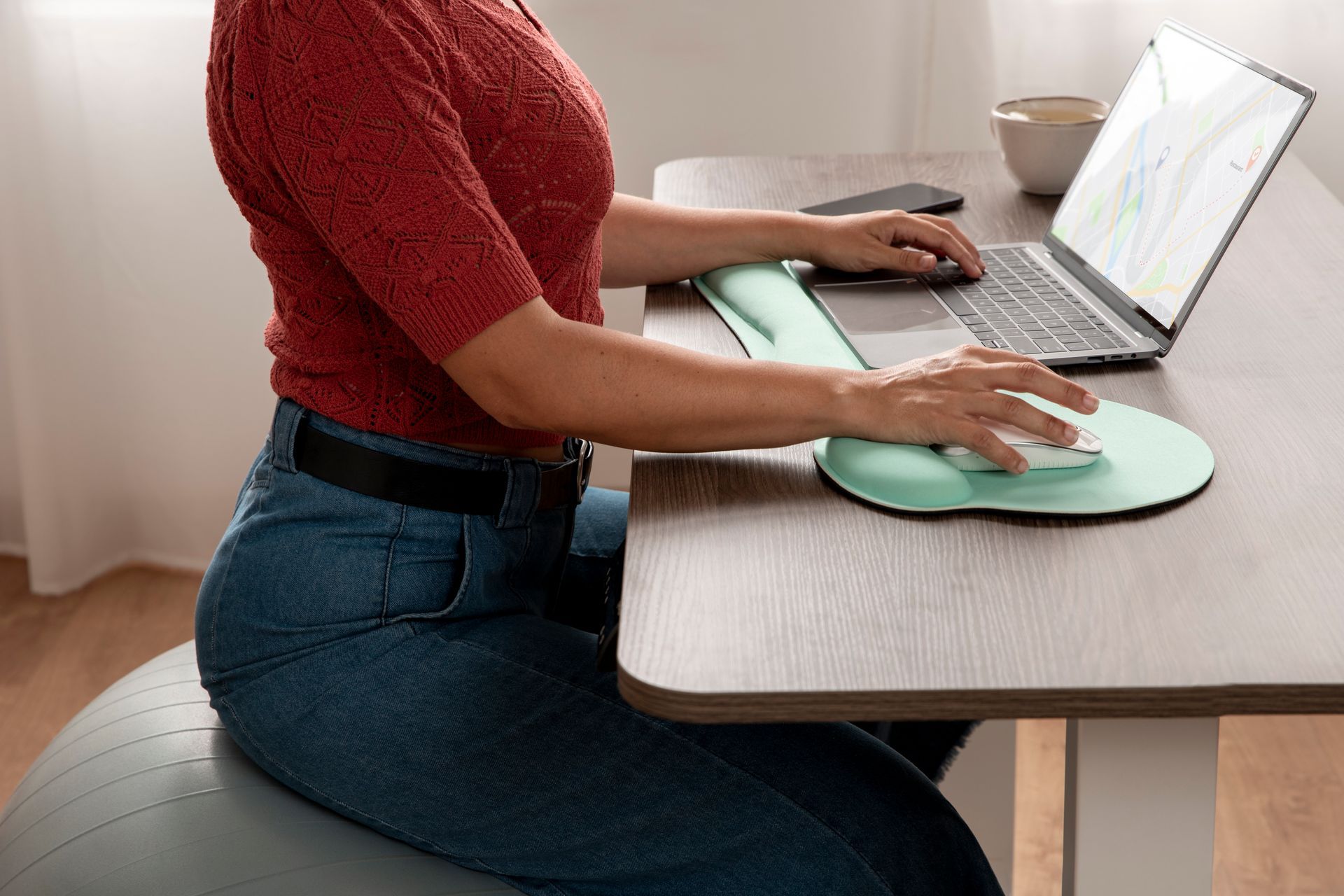 A woman is sitting on a ball at a desk using a laptop computer.