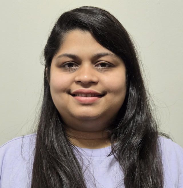Riya with dark hair and a light purple shirt smiles at the camera.