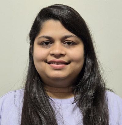 Riya with long dark hair and a light purple shirt smiles at the camera.