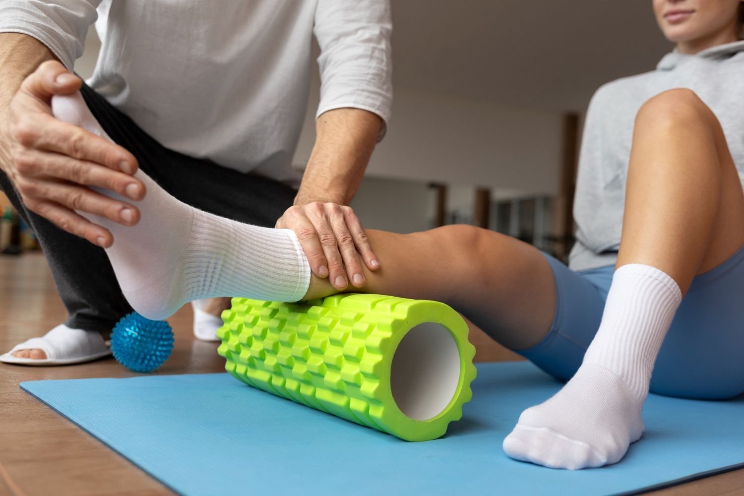 A man is stretching a woman 's leg with a foam roller.