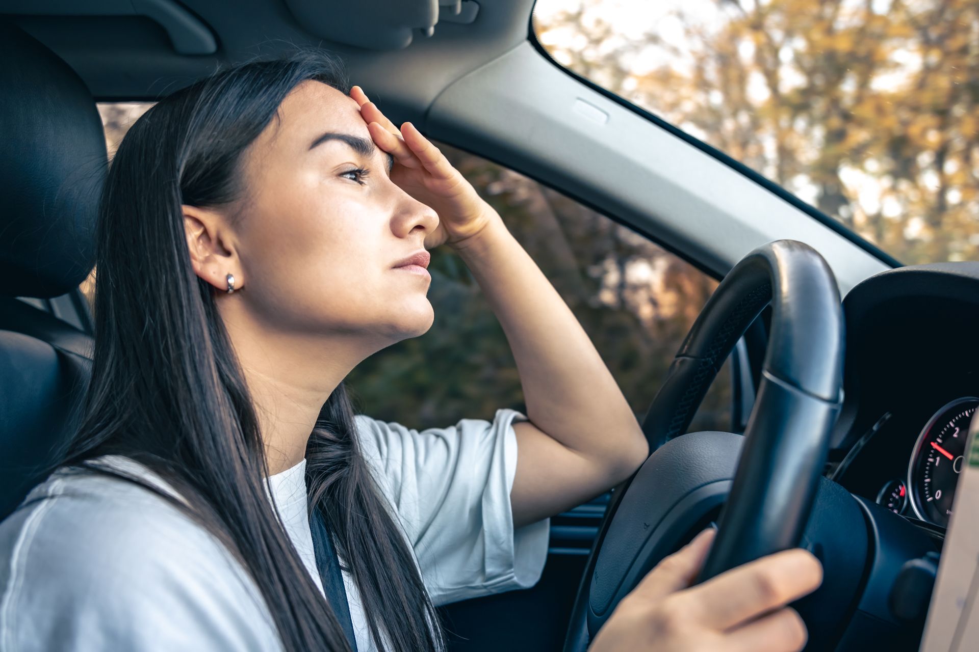 Driver rubbing her forehead while steering a car, appearing tired or stressed
