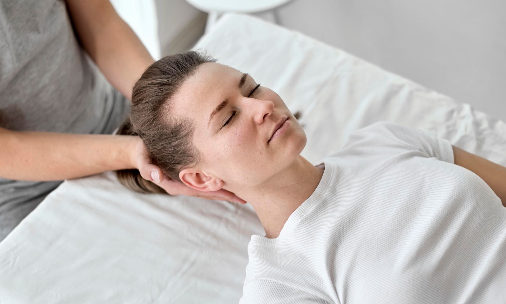 A woman is laying on a bed getting a head massage.