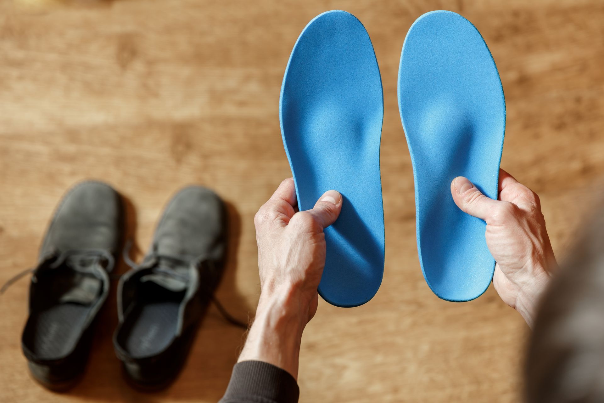 Hands holding blue shoe insoles; a pair of black shoes are in the background.