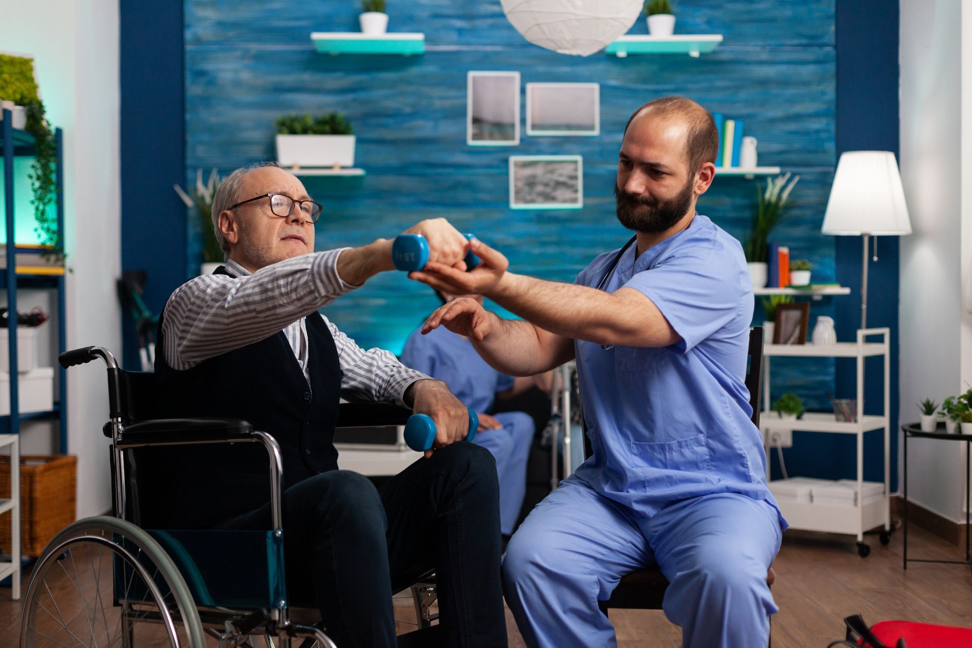 Man in wheelchair lifts weights with help of caregiver. Blue walls, neutral setting.
