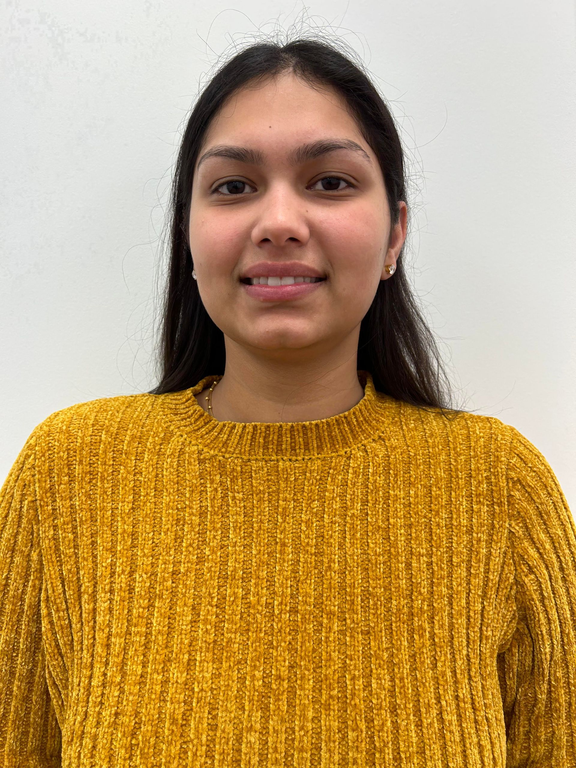 Jasmeen wearing a yellow sweater is smiling for the camera.