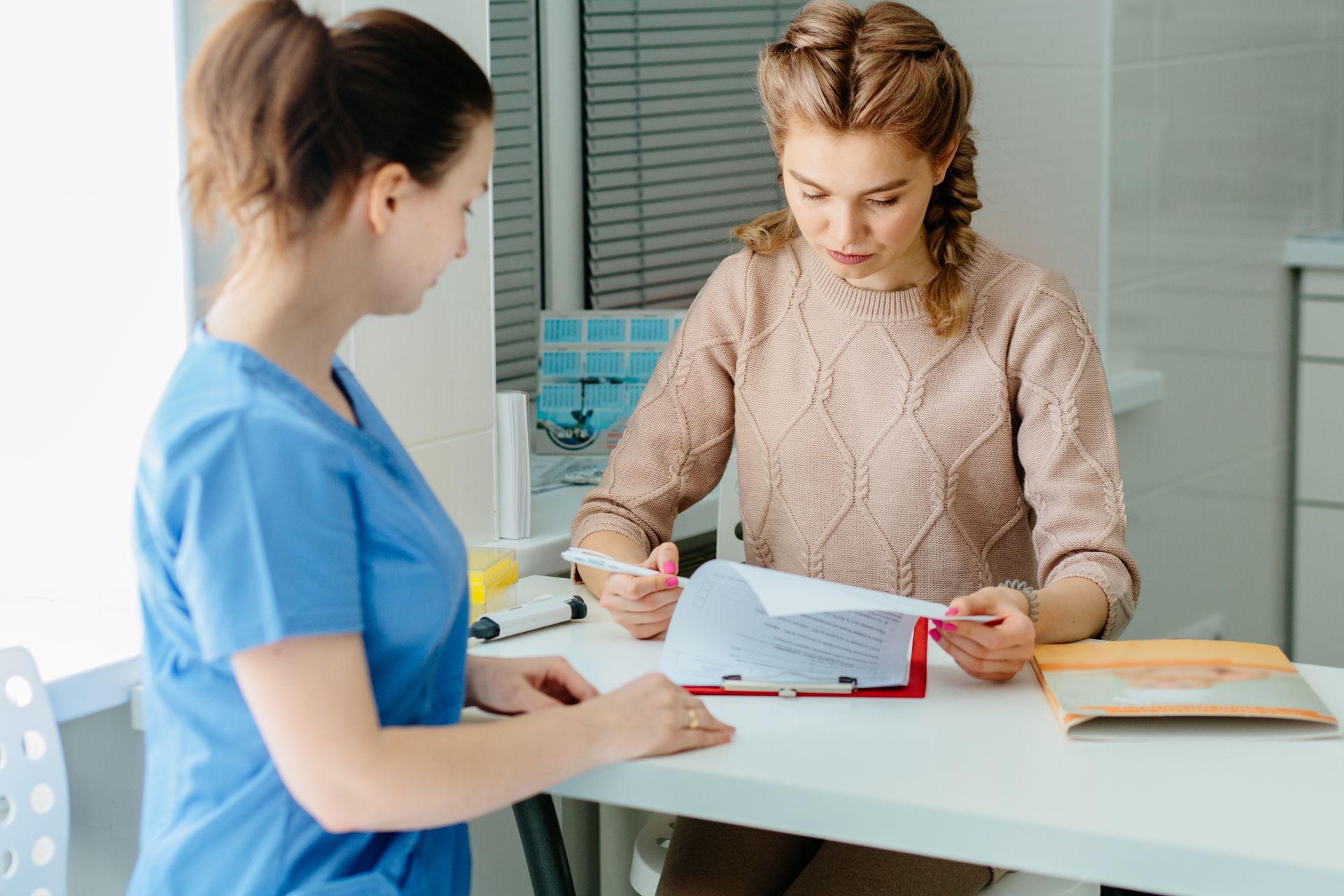 Woman reviewing paperwork with a healthcare worker at a reception desk.