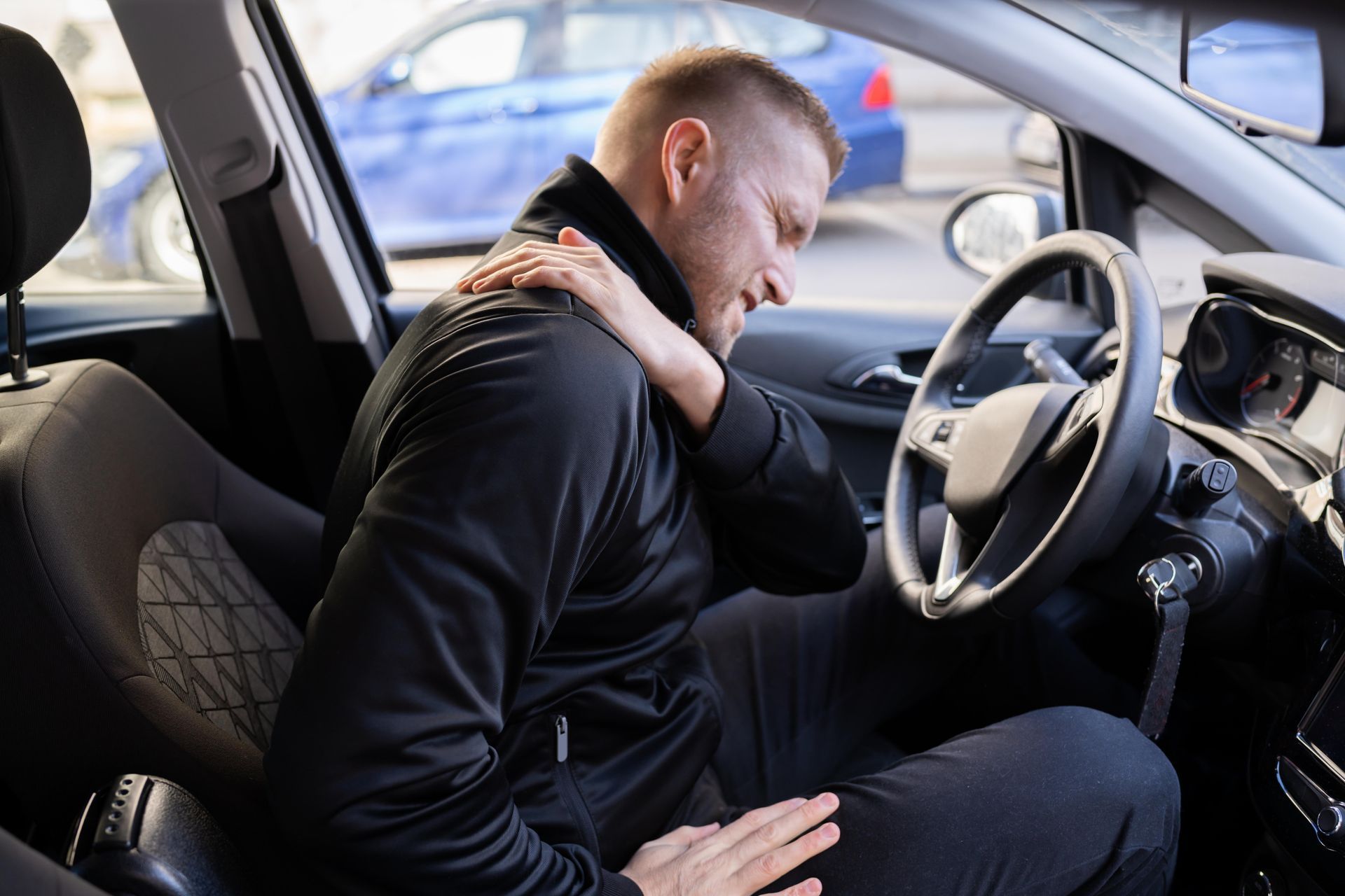Man in car clutching shoulder, appearing in pain after a car accident.