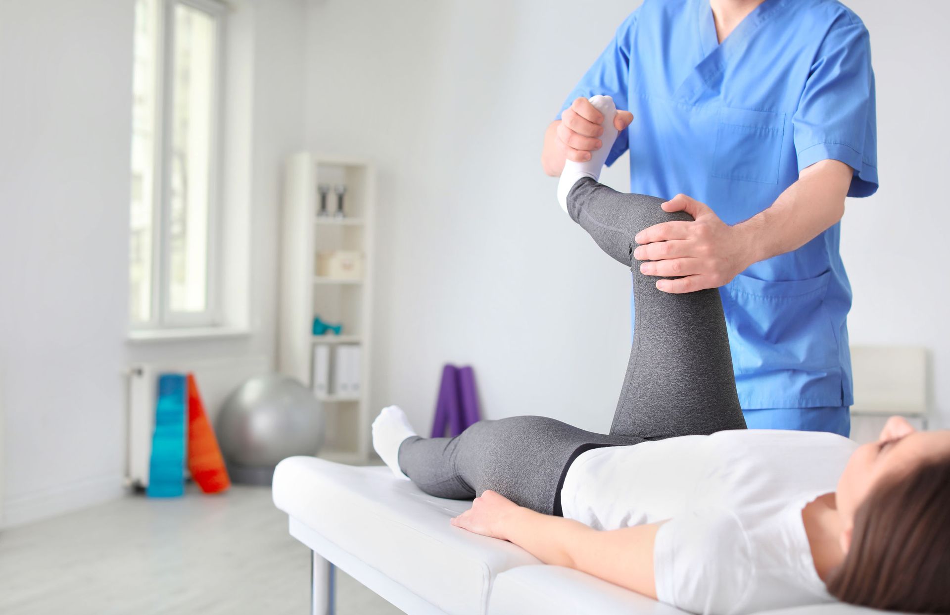 A woman is laying on a bed getting her leg examined by a doctor.