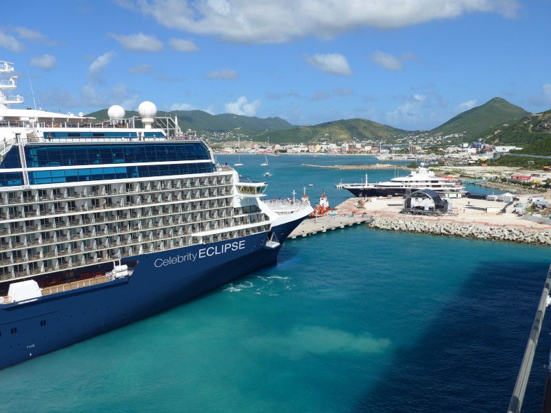 Large cruise ship docked in turquoise water, harbor in background under blue sky.