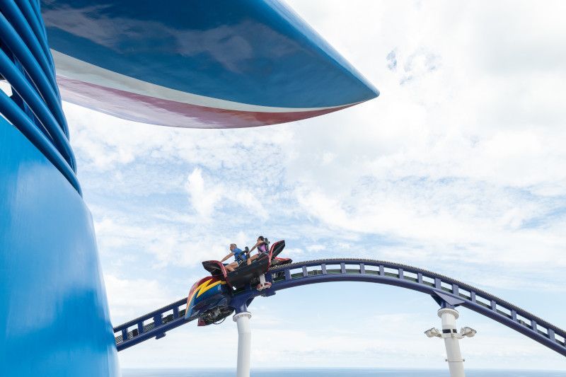 Roller coaster on a ship track against a blue sky, passengers are on the coaster.