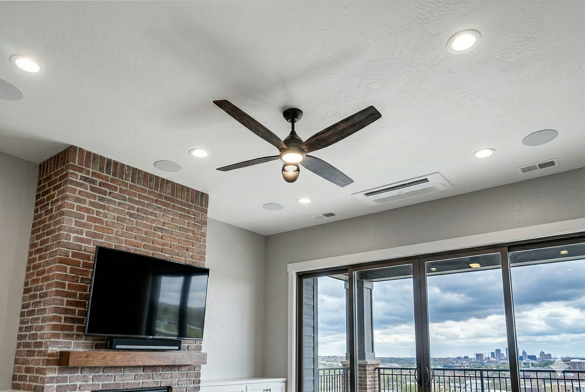 Living room with a dark ceiling fan, recessed lights, exposed brick fireplace, and sliding glass doors with a city view.