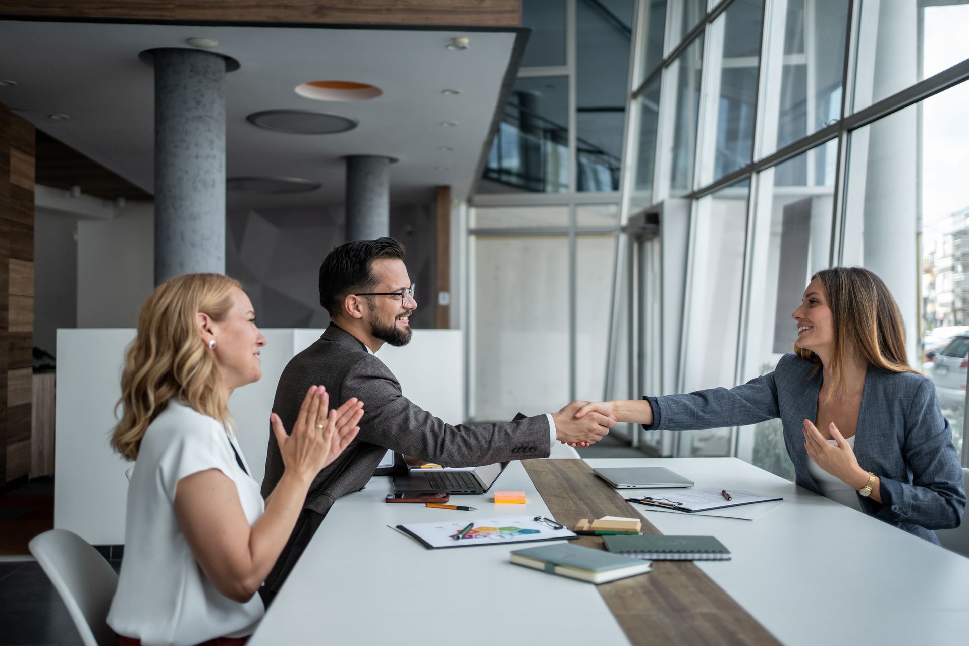 People shaking hands at a table in a modern office, one person clapping. People shaking hands at a table in a modern office, one person clapping.