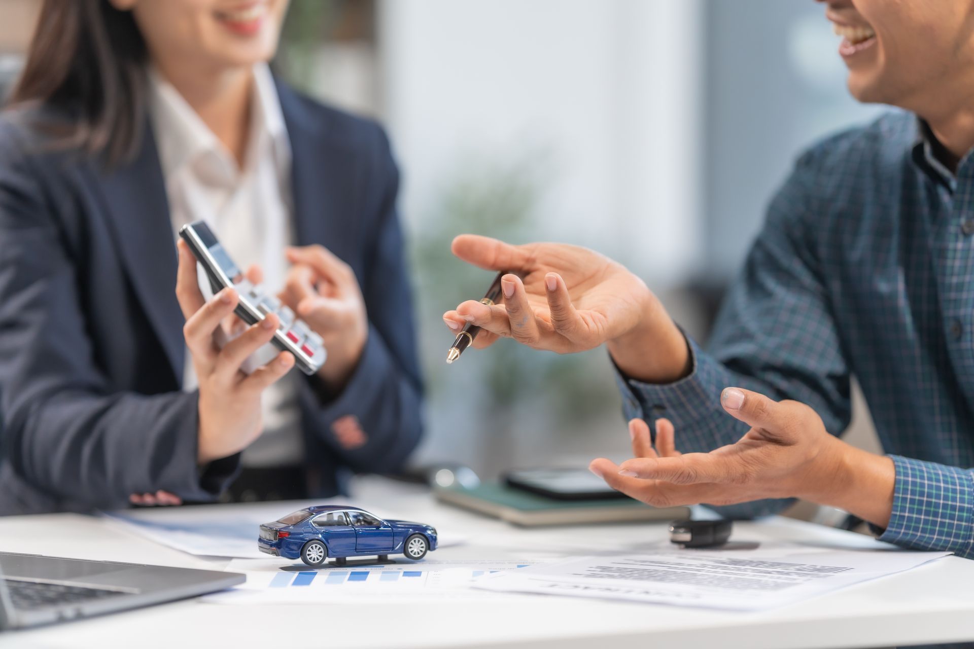 Person in a blue shirt hands keys to another. A person in a blazer holds a phone. A toy car sits on a desk. Person in a blue shirt hands keys to another. A person in a blazer holds a phone. A toy car sits on a desk.