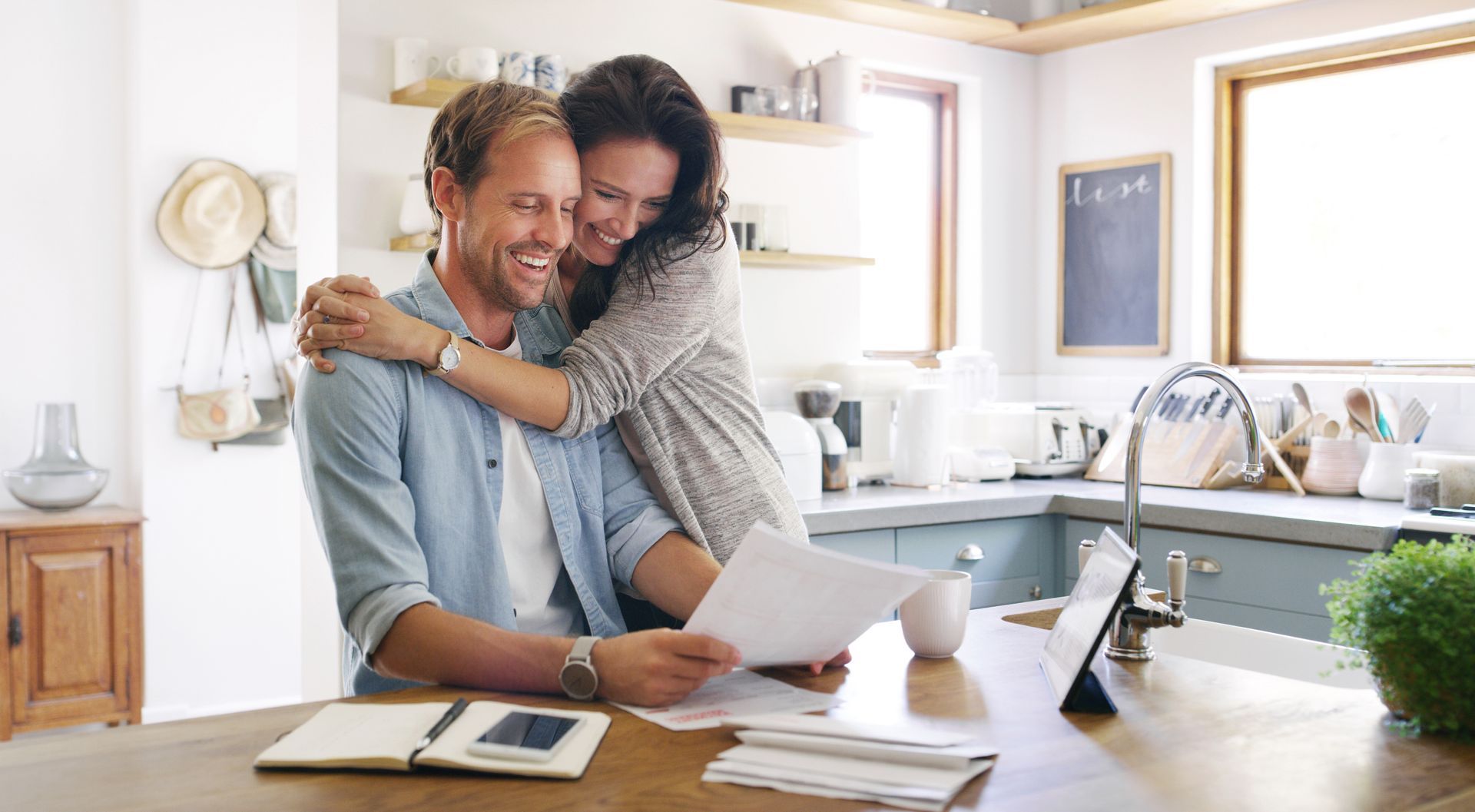 Couple smiles and embraces over documents in a modern kitchen. Couple smiles and embraces over documents in a modern kitchen.