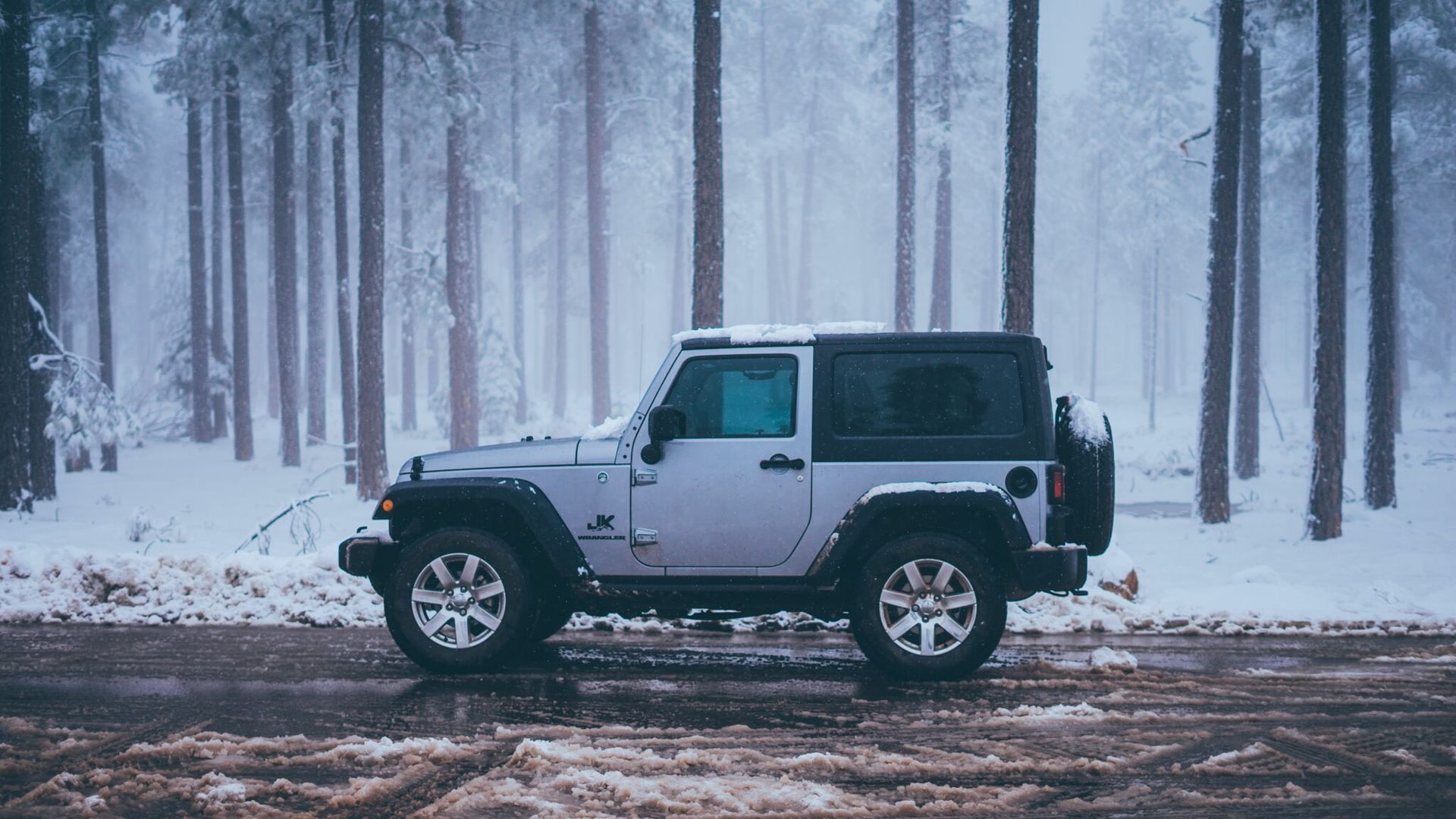 A white jeep is parked on a snowy road in the woods.