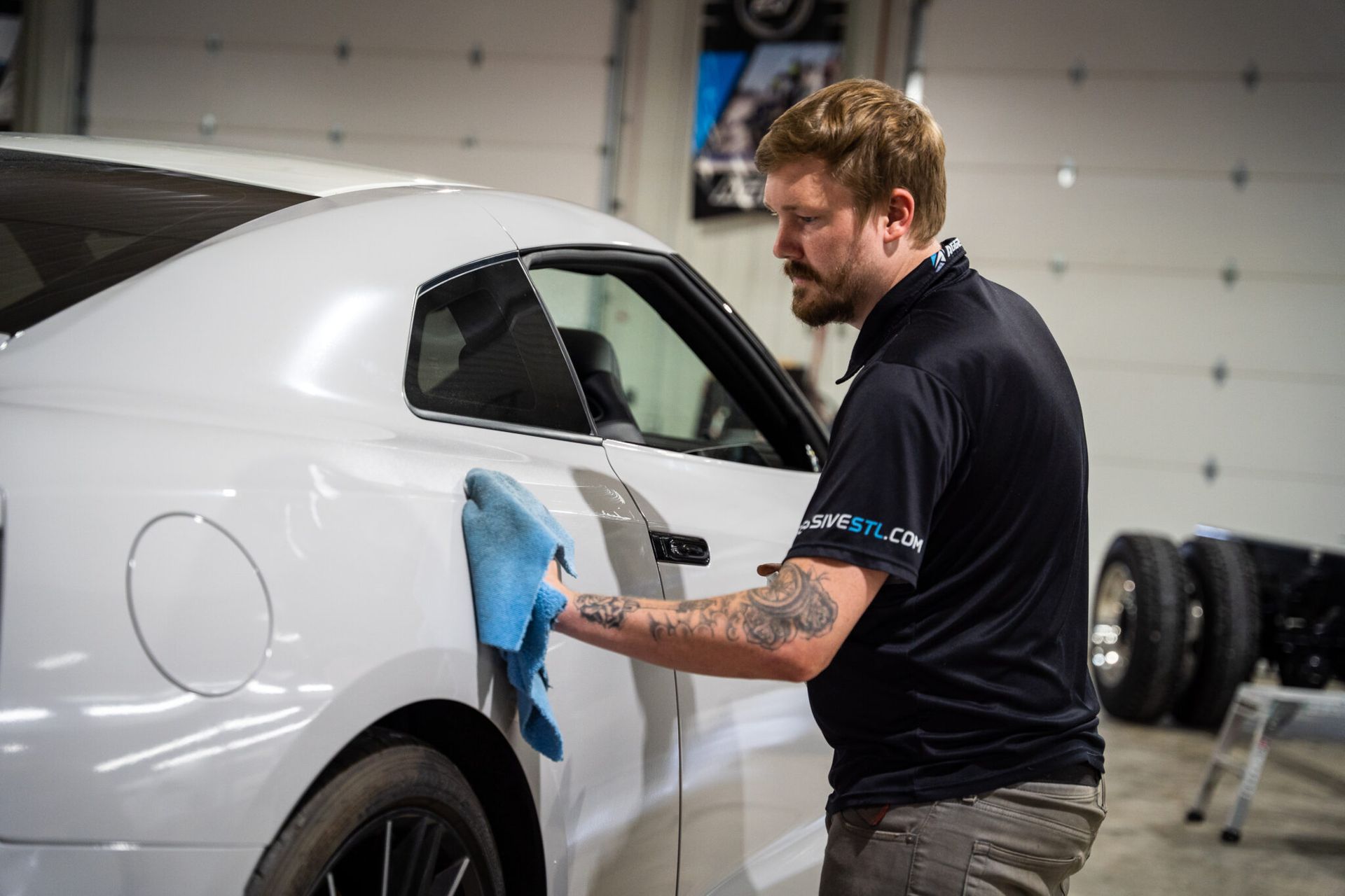 A man is cleaning a white car with a cloth in a garage.