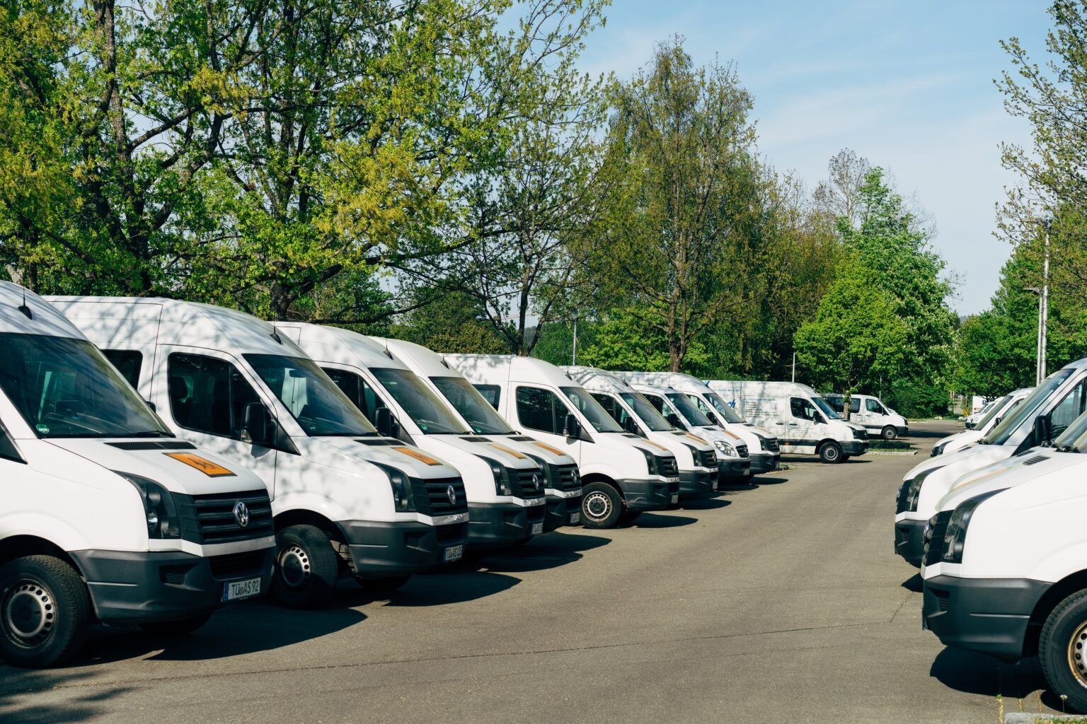 A row of white vans are parked in a parking lot.