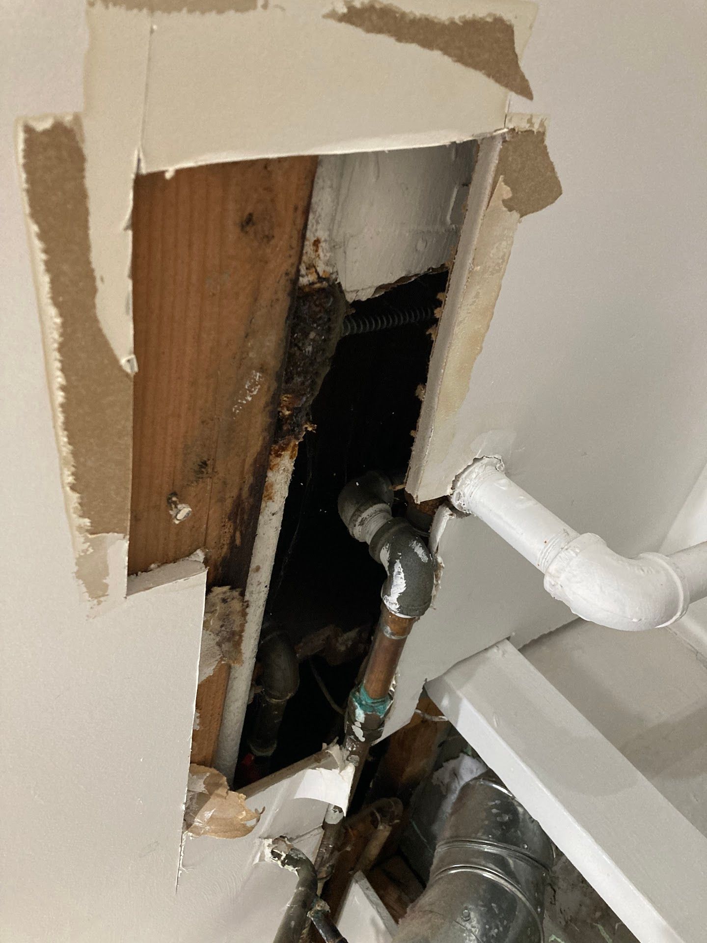 Hole in ceiling reveals pipes and water damage; brown wood, white ceiling, and a dark space.