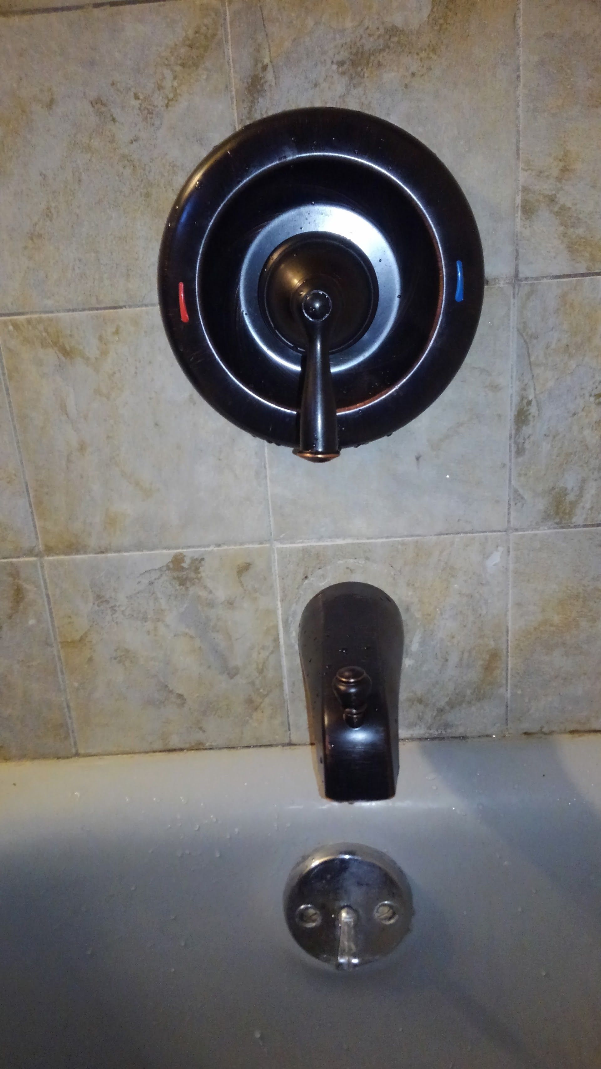 Bathtub faucet with a single handle and diverter spout, mounted on tiled wall.