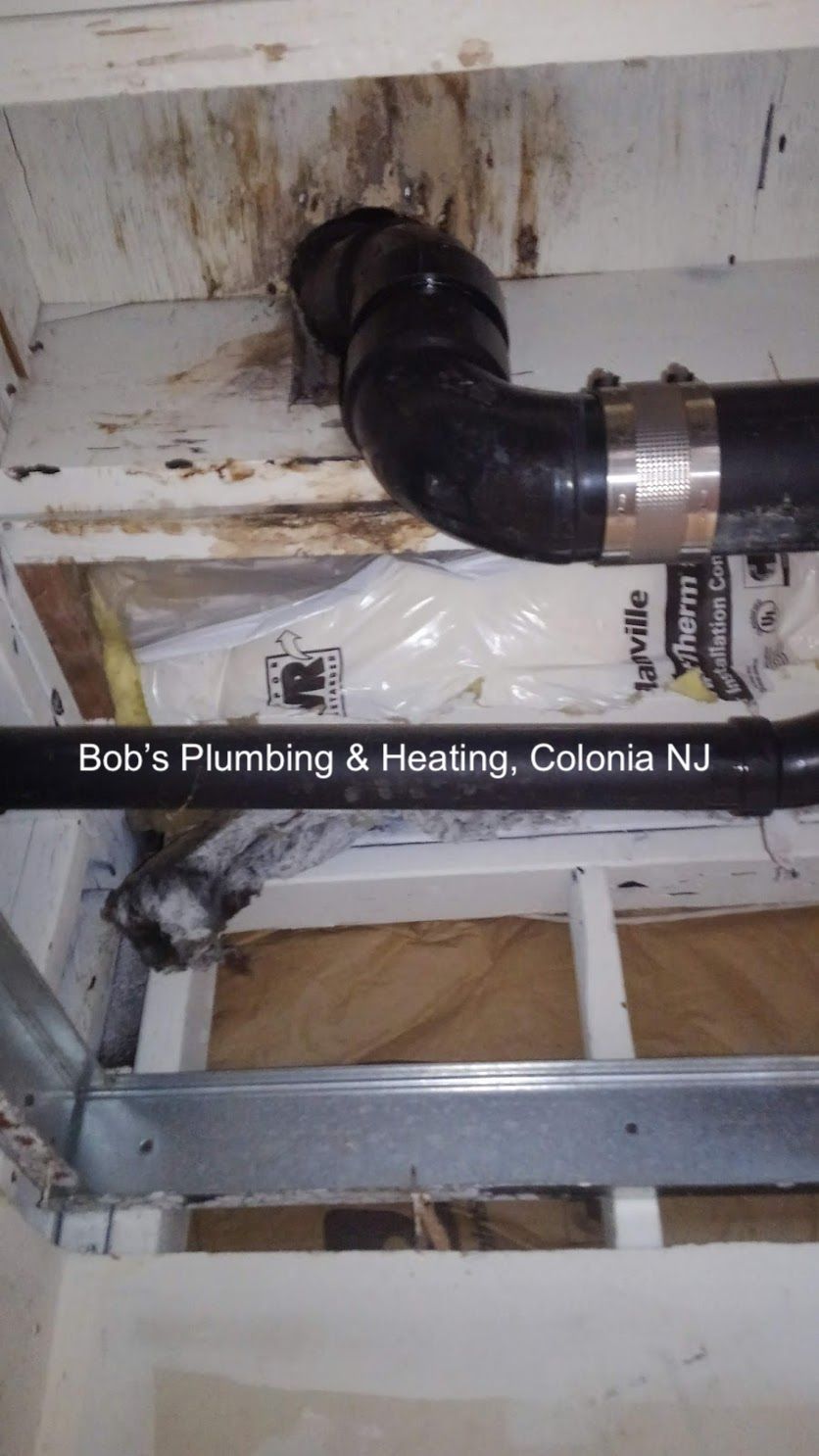 Black plumbing pipes with a leak against wooden beams, insulation visible.