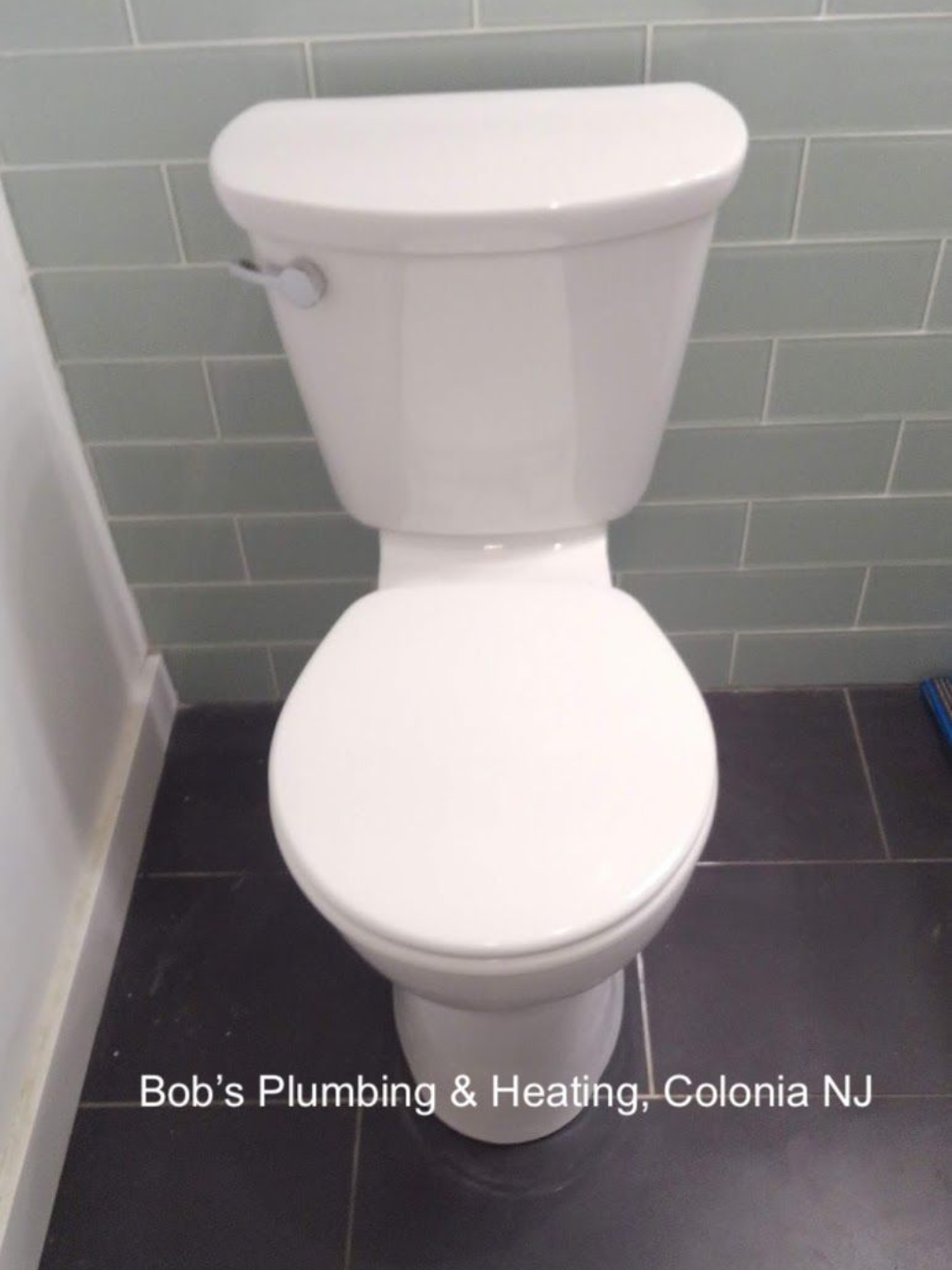 White toilet in a bathroom with blue-green tiled wall and dark floor.