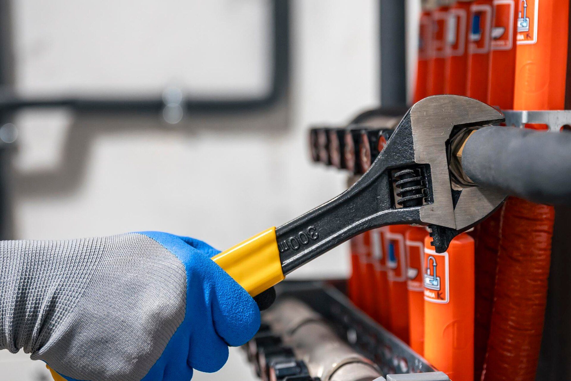 Gloved hand using a wrench to tighten a pipe in front of orange equipment.