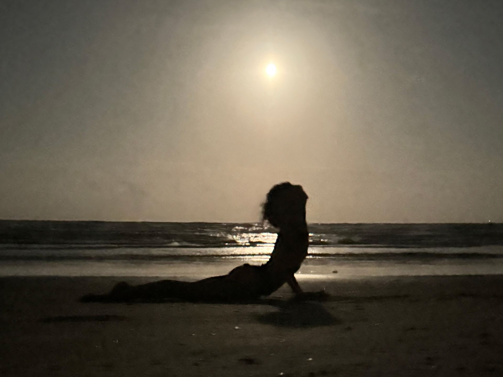 A woman is doing yoga on the beach at sunset