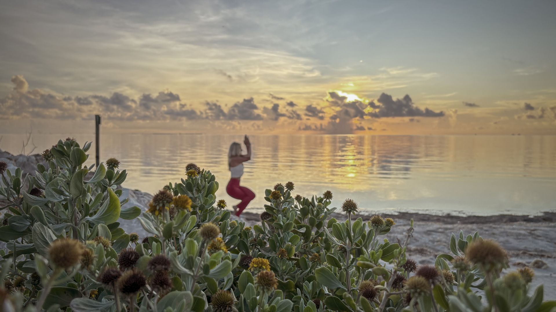 A woman is doing yoga on the beach at sunset.