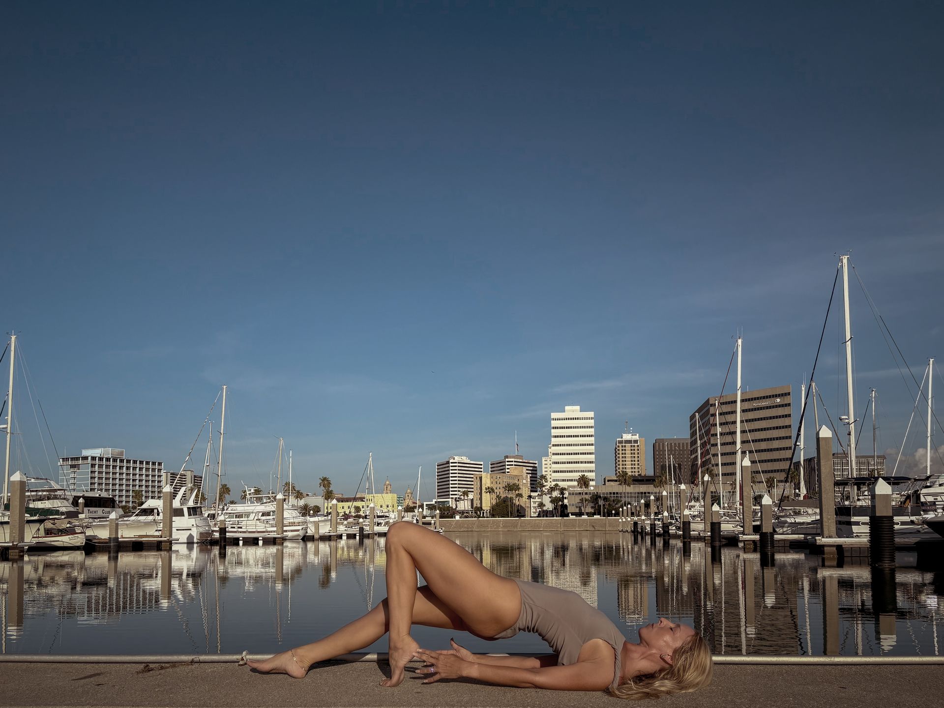 A woman is laying on the ground in a somatic yoga pose in front of a body of water.