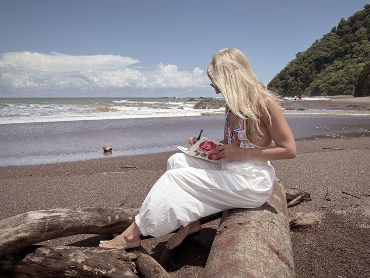 A woman is sitting on a log on the beach writing in a notebook