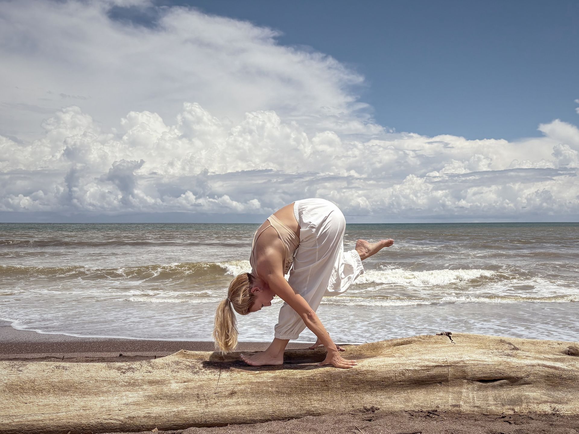 A woman is doing yoga on the beach near the ocean.