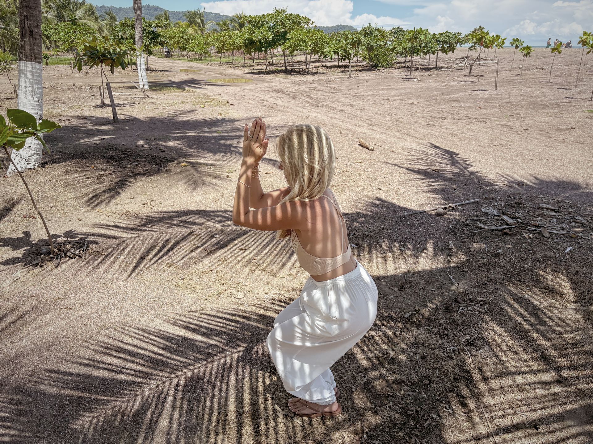 Woman doing yoga pose outdoors in sunny, sandy area with shadow patterns.