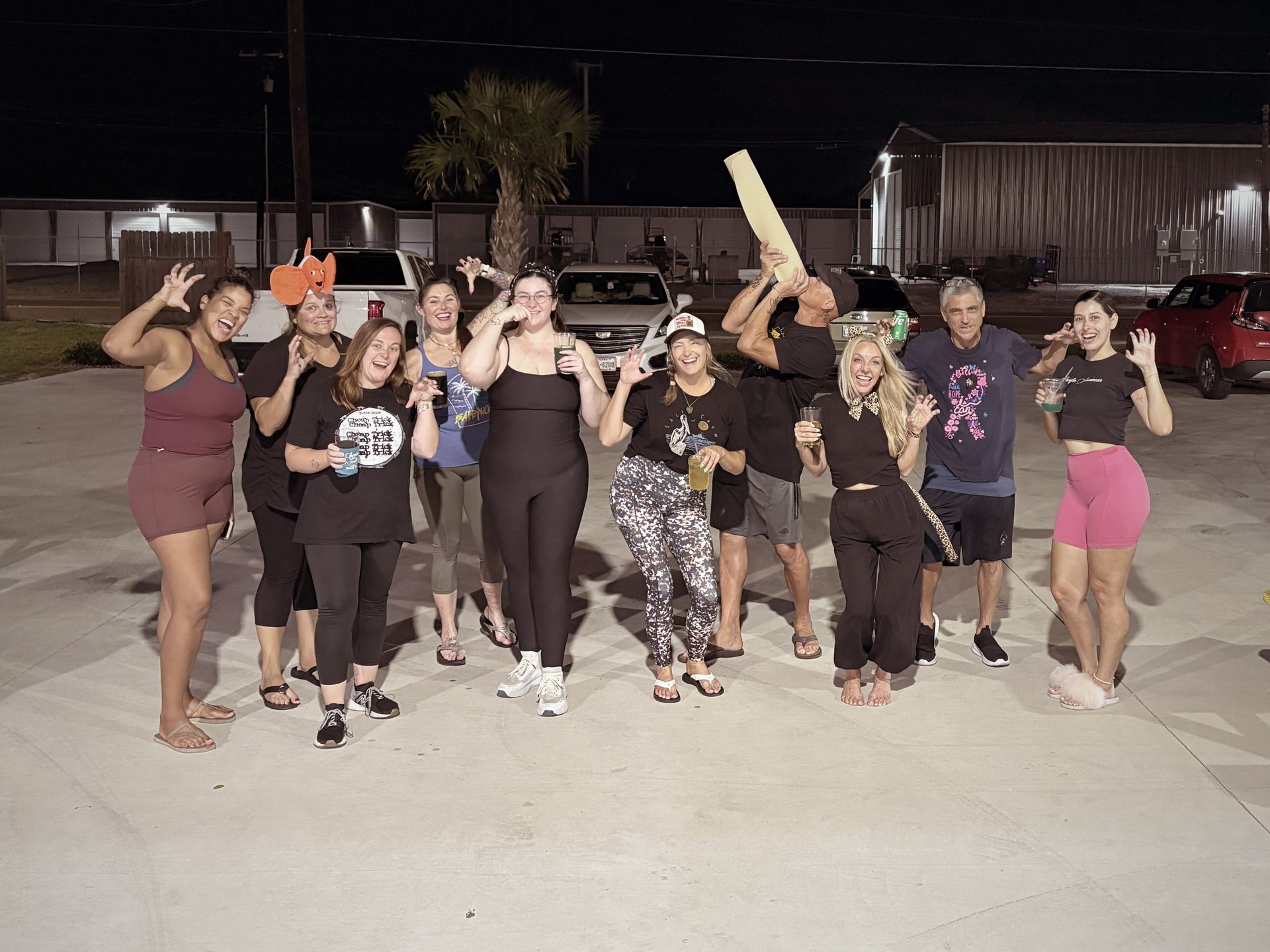 Group of people posing outdoors at night, waving and smiling.