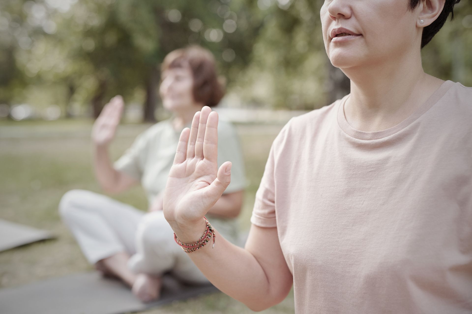 Two people practicing yoga outdoors with hands raised.