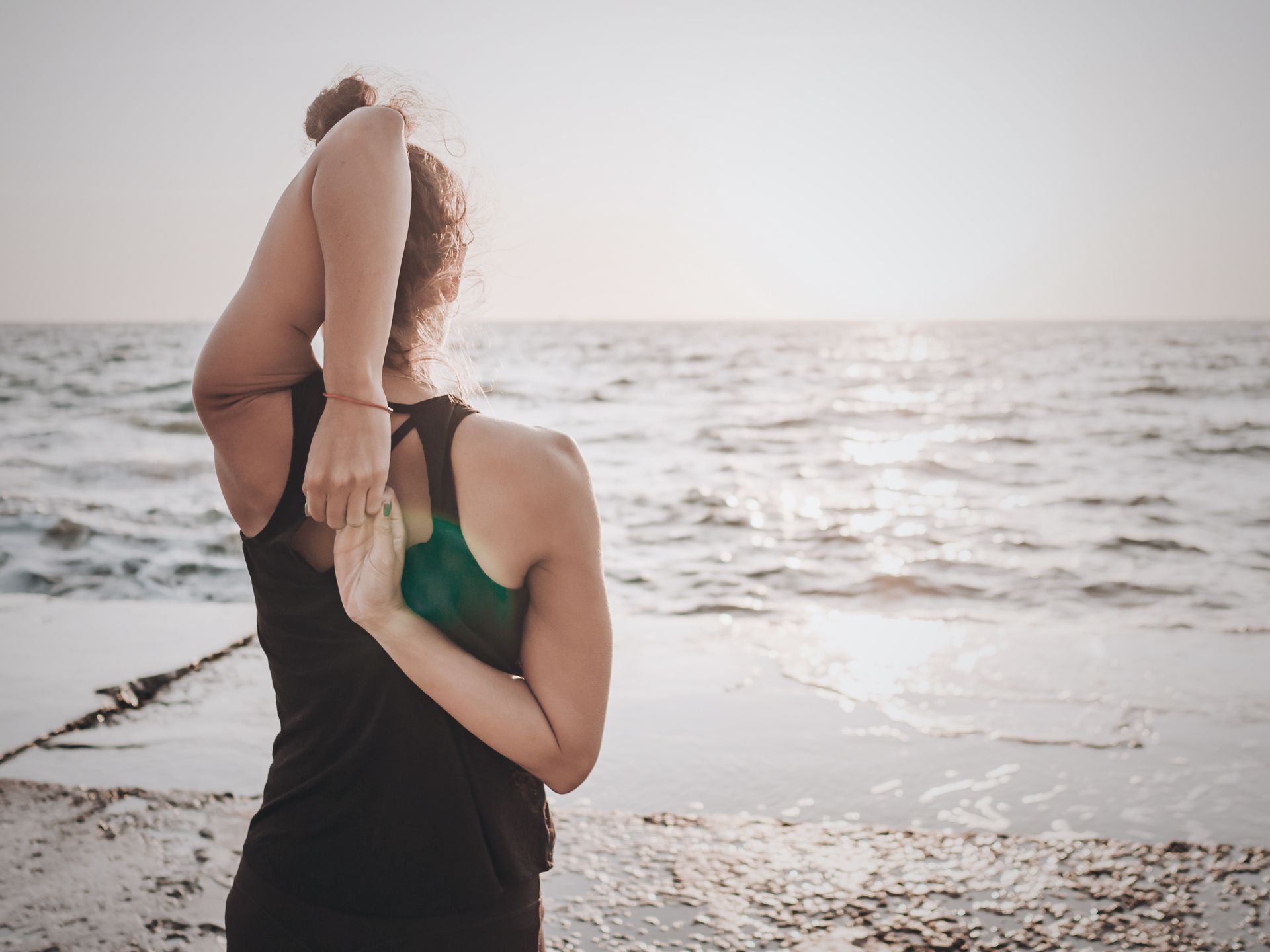 Woman stretching arms behind back on a beach.