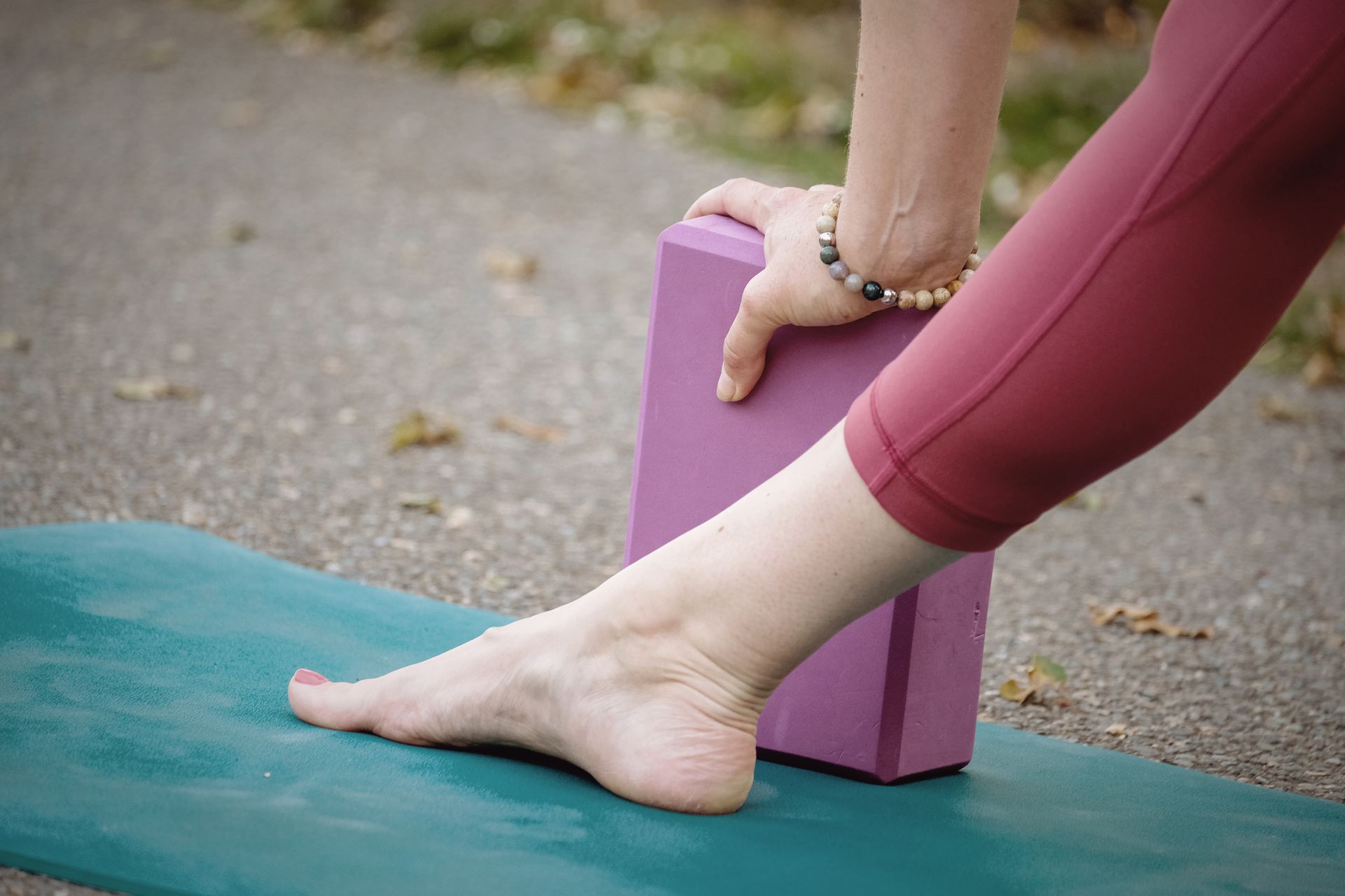 Person's foot and hand on a yoga block and mat, stretching the leg. Purple leggings and block.