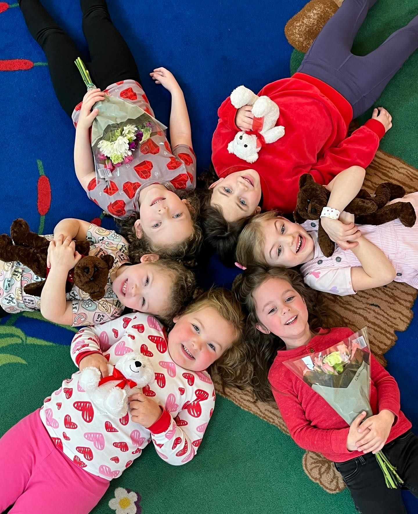 A group of young girls are laying in a circle on the floor holding stuffed animals and flowers.