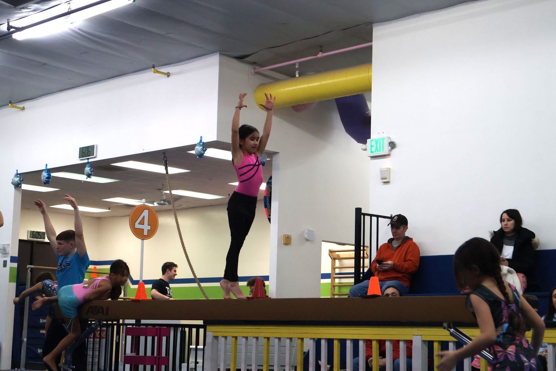 A girl is standing on a balance beam in front of a sign that says 4