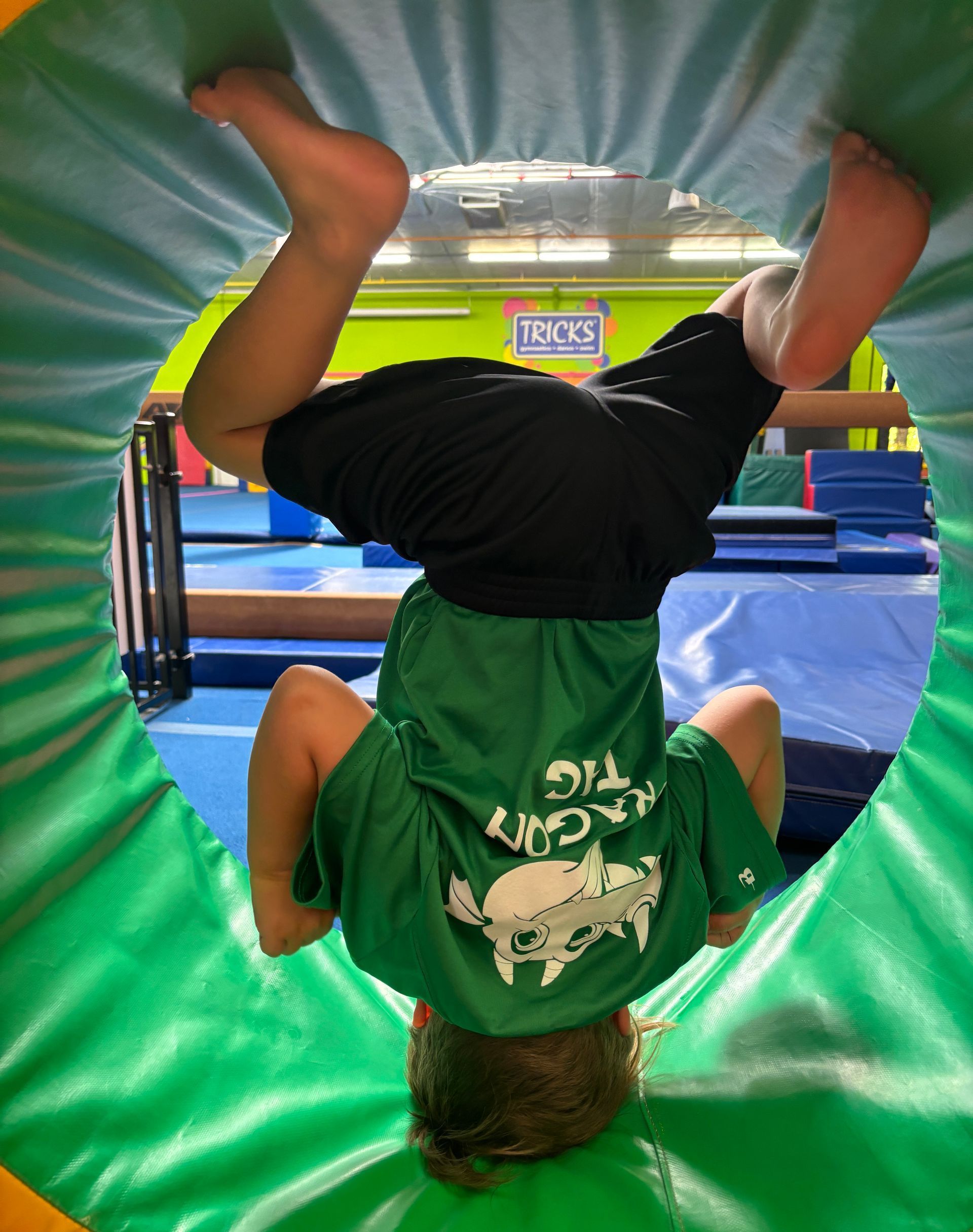 A young boy in a green shirt is doing a handstand in a gym.