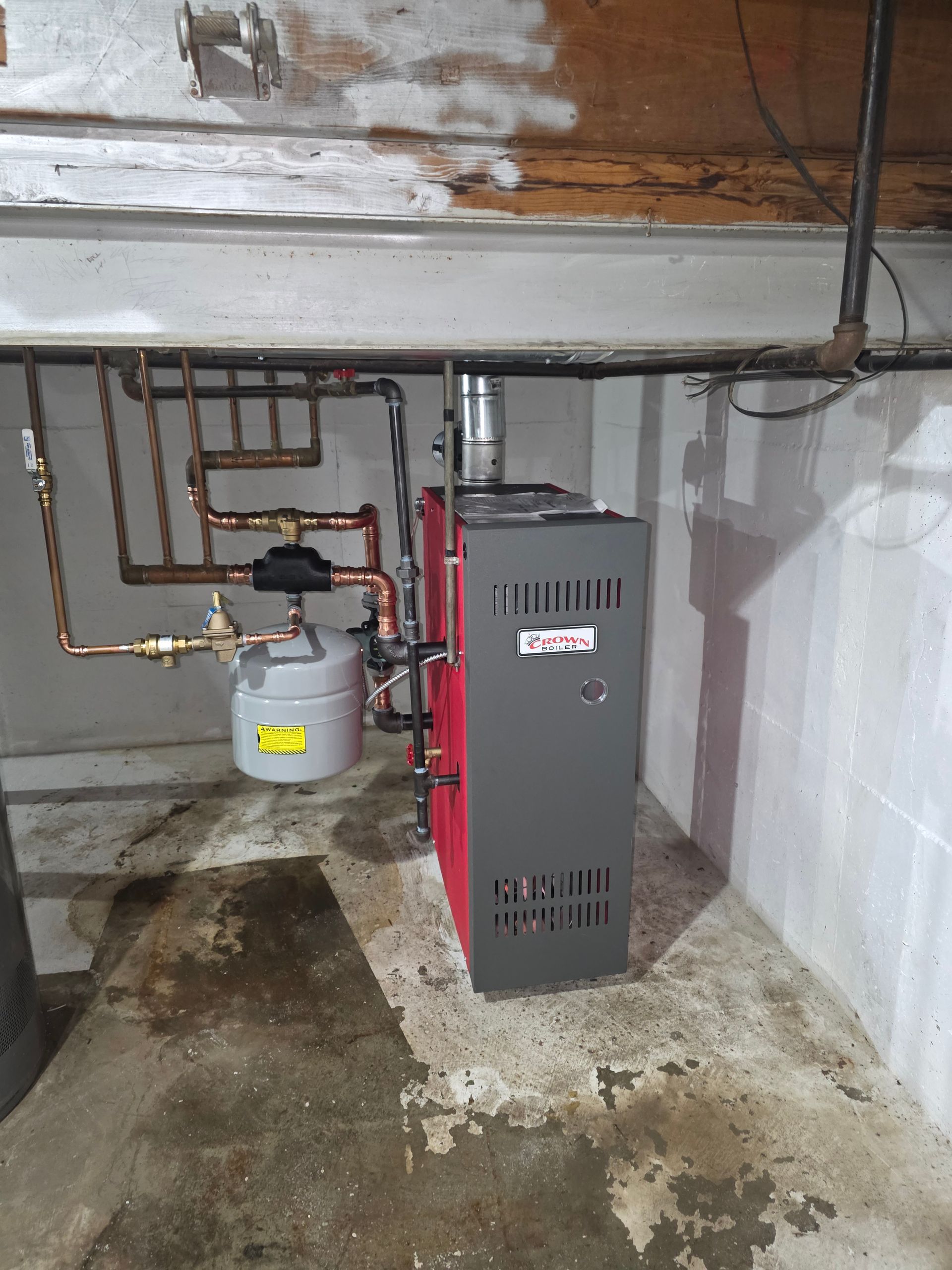 A water heater is sitting in a room next to a brick wall.