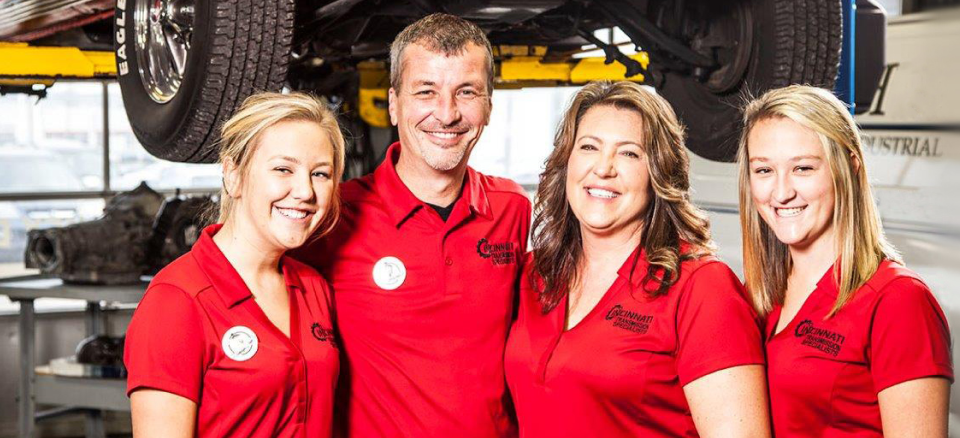 A group of people in red shirts are posing for a picture in a garage | Cincinnati Transmission Specialists & Sharon Woods Auto Care
