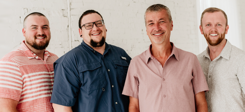 A group of four men are standing next to each other and smiling | Cincinnati Transmission Specialists & Sharon Woods Auto Care