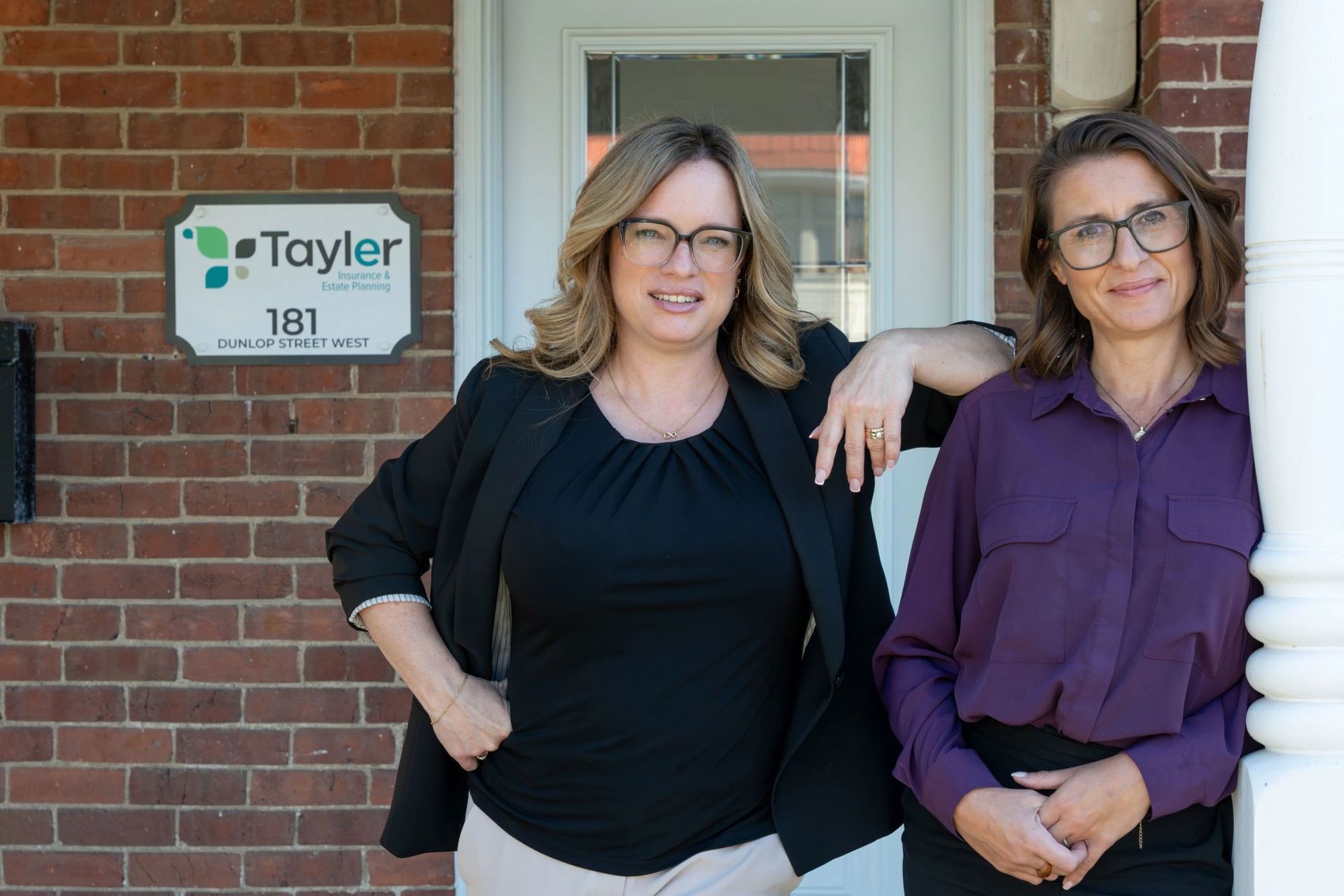 Woman in blazer reviews paperwork with couple at a table; laptop, plant, and pens are present.