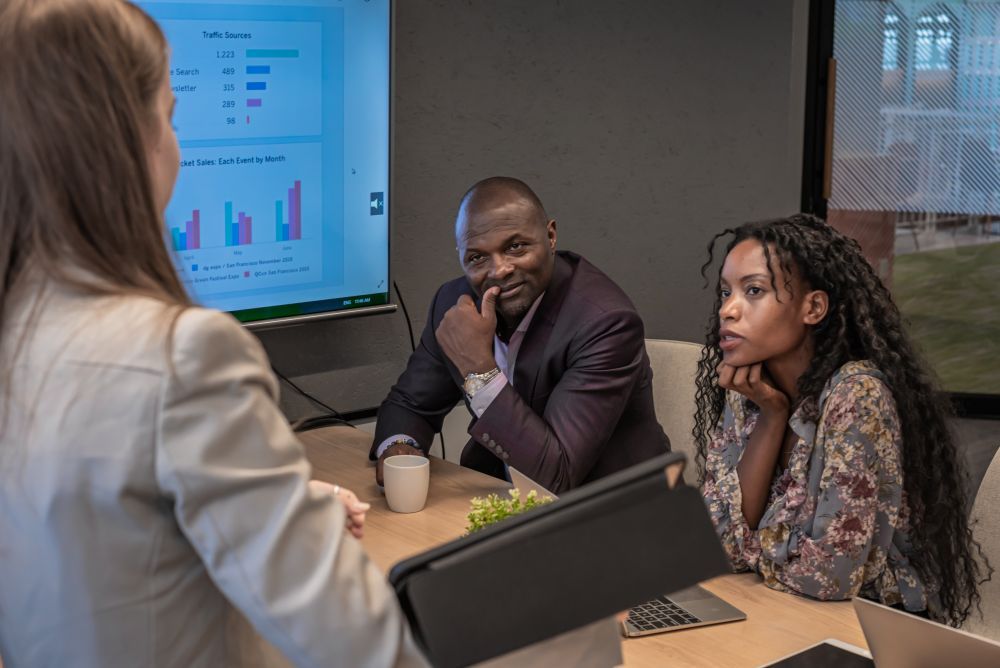 Two people reviewing documents at a table; laptop open displaying a graphic; glasses nearby.