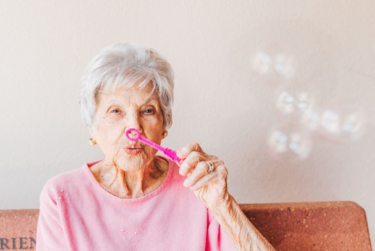 Estate Planning - An elderly woman is blowing soap bubbles while sitting on a couch.