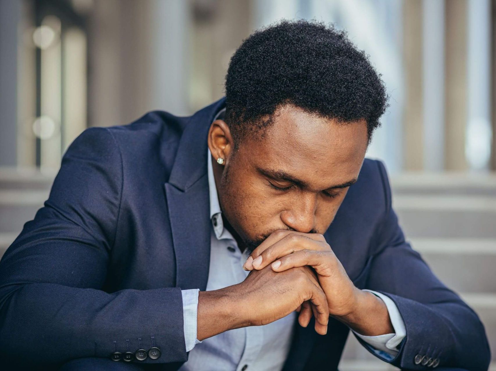 A man in a suit is sitting down with his hands on his chin.