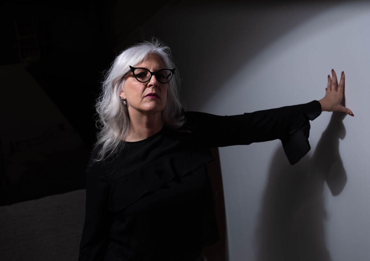 Financial Planning - A woman with white hair and glasses is leaning against a wall.
